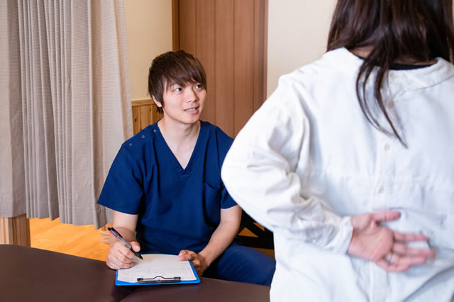 Correct整体院の院長 山口朋宏が腰の痛い女性の患者様に丁寧に検査、問診をしている写真